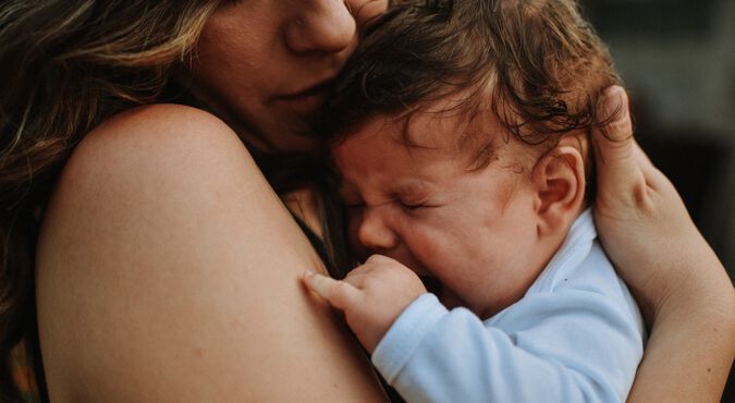 Bebê chorando no colo da mãe e sendo amparado