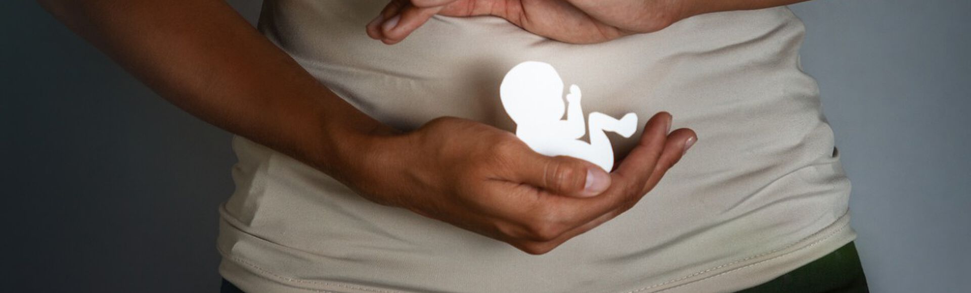 Visão de mulher mostrando a maquete de um bebê em frente a seu ventre.