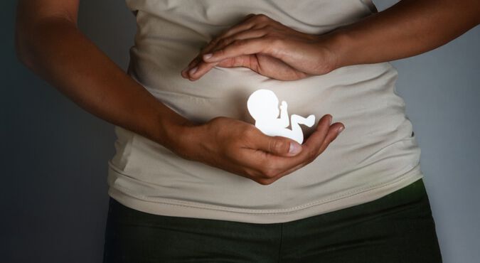Visão de mulher mostrando a maquete de um bebê em frente a seu ventre.