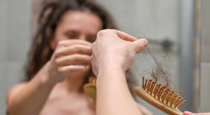 Mulher segurando escova de cabelo cheia de fios de cabelo