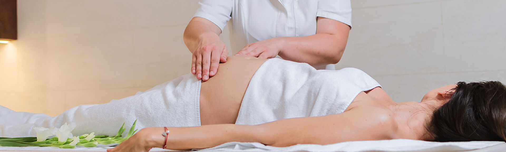 Mulher grávida deitada recebendo massagem na barriga