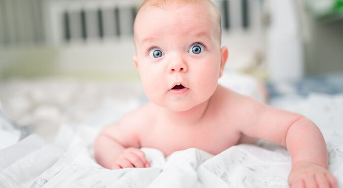 Bebê branco deitado de bruços com olhos azuis bem abertos