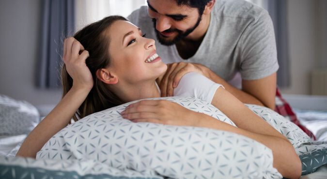 Casal sorridente deitado na cama e homem massageando mulher