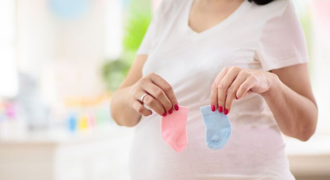 Mulher grávida segurando meias de bebê em azul e rosa em frente da barriga