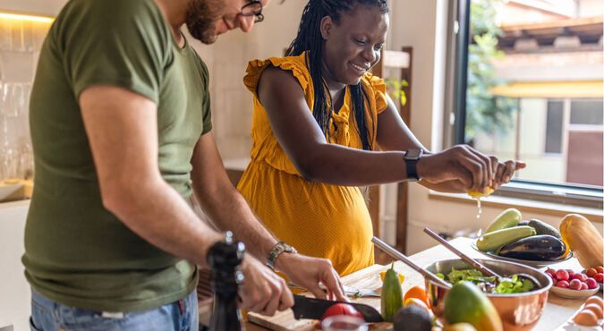 Mulher negra grávida e homem branco cozinhando juntos