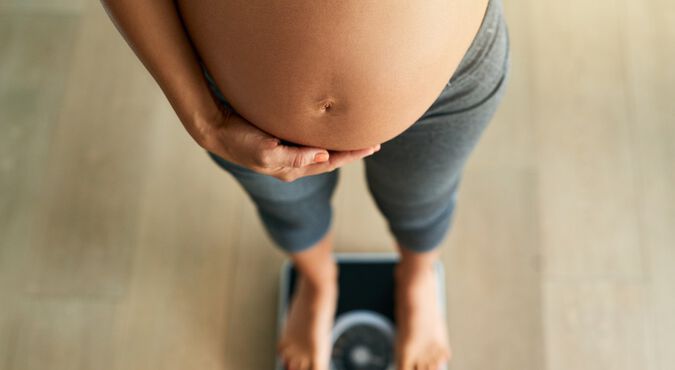 Mulher grávida com barriga em evidência sobre balança