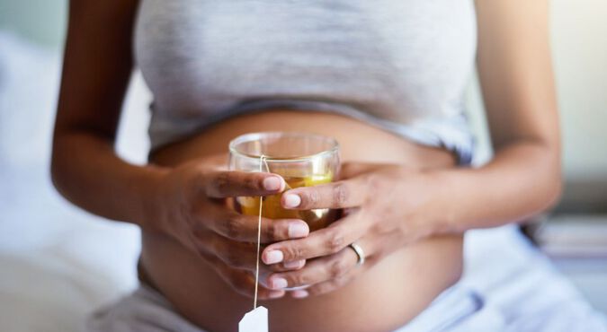 mulher grávida segurando xícara de chá em frente à barriga