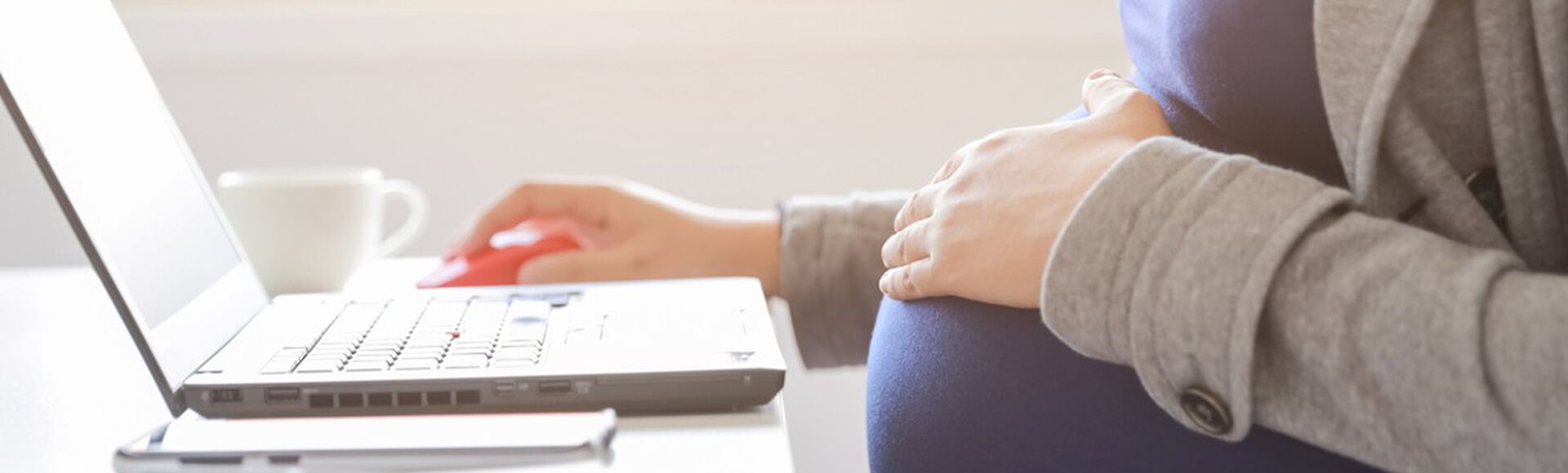 Mulher grávida sentada em mesa de trabalho digitando em computador