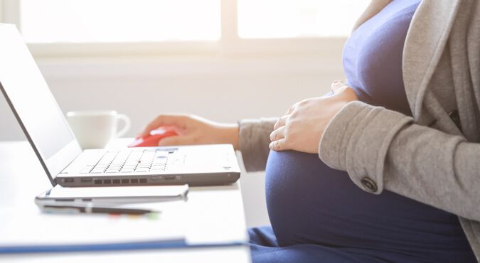 Mulher grávida sentada em mesa de trabalho digitando em computador