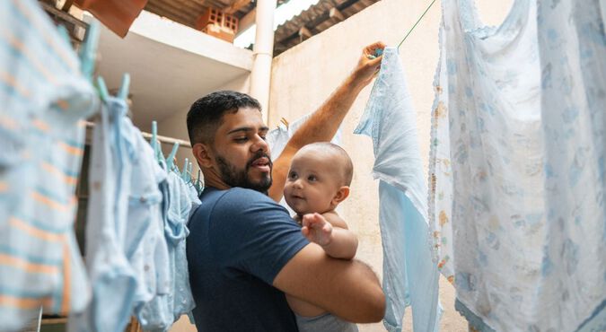 Pai cuidando do filho bebê enquanto pendura roupas no varal