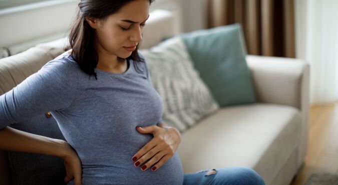 Mulher grávida com maos na barriga em sinal de desconforto