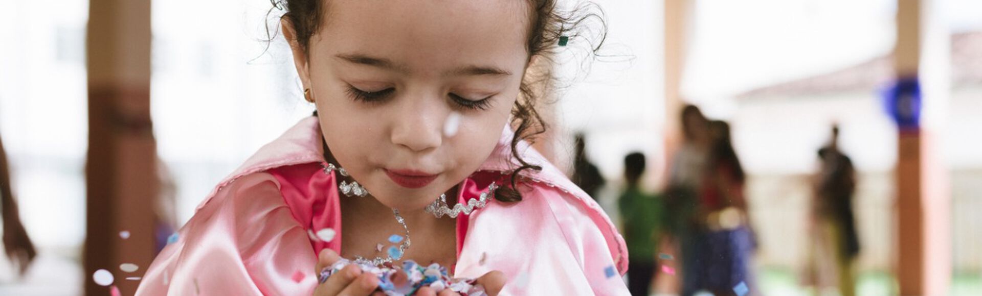 Menina fantasiada soprando confete durante no bloquinho infantil