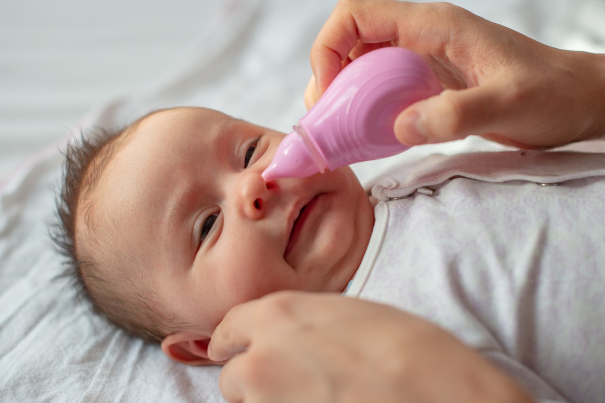 Cuidador realizando higiene nasal em bebê com aspirador nasal
