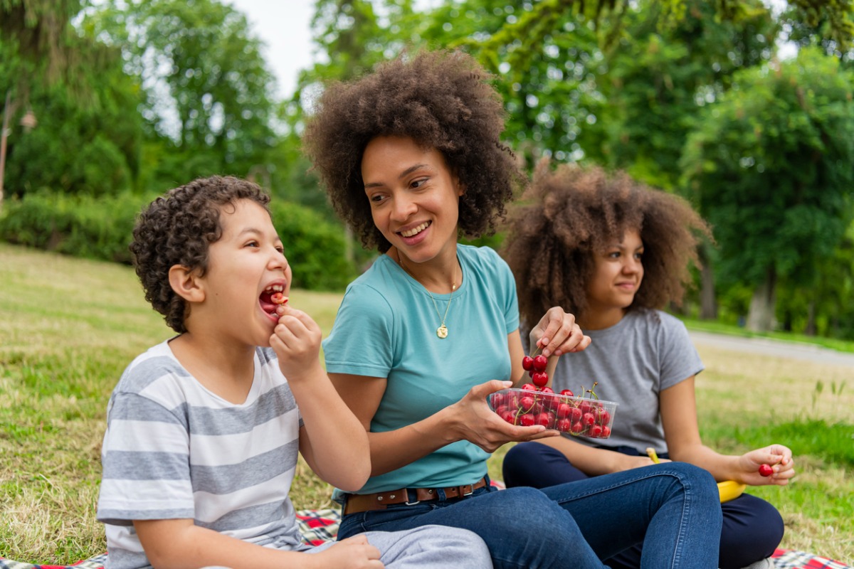 Mãe sentada na grama com os filhos enquanto comem frutas